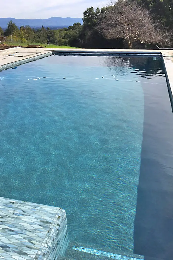 Remodeled Swimming Pool With Clear Blue Water And Dark Coping, Surrounded By Mountains And Trees