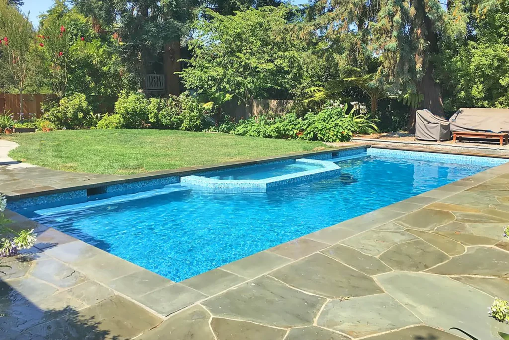Remodeled Swimming Pool With Blue Interior Finish, Built-In Bench Seating, And Natural Stone Patio Decking