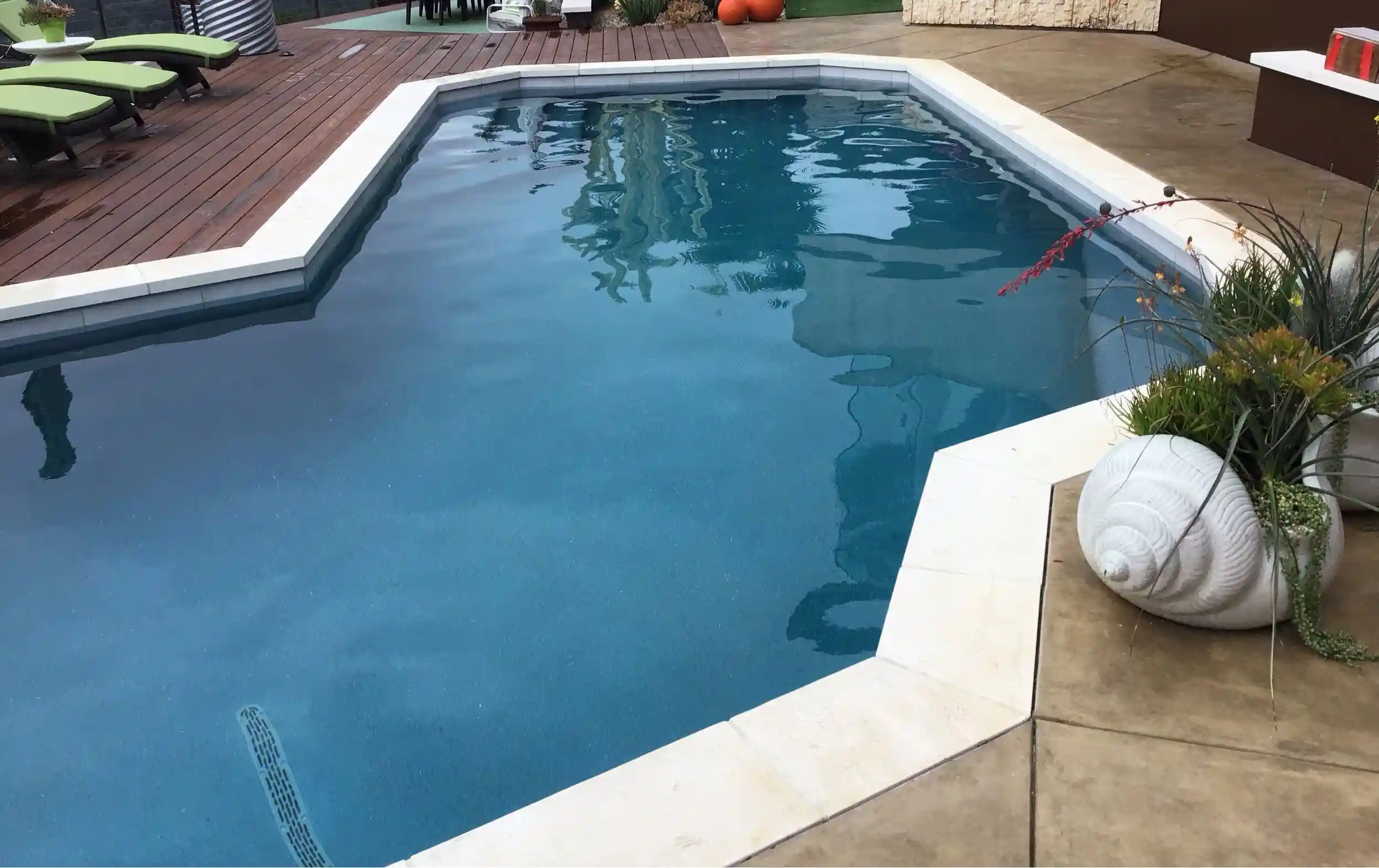 Remodeled Swimming Pool With Bright Blue Water, White Coping, And Surrounding Concrete Patio And Wooden Deck